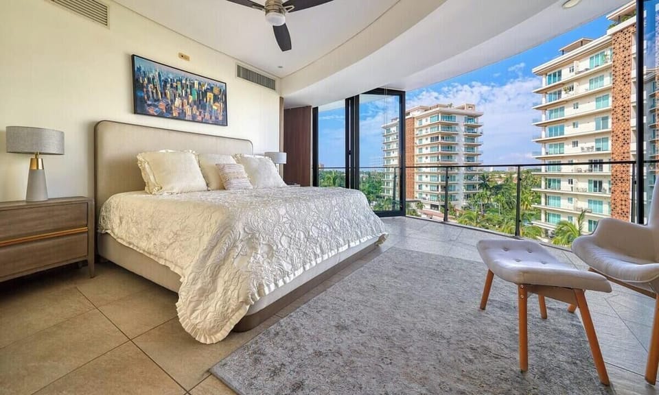 Luxurious bedroom showcasing a king bed, a sleek ceiling fan, and large glass doors opening to a scenic city balcony.