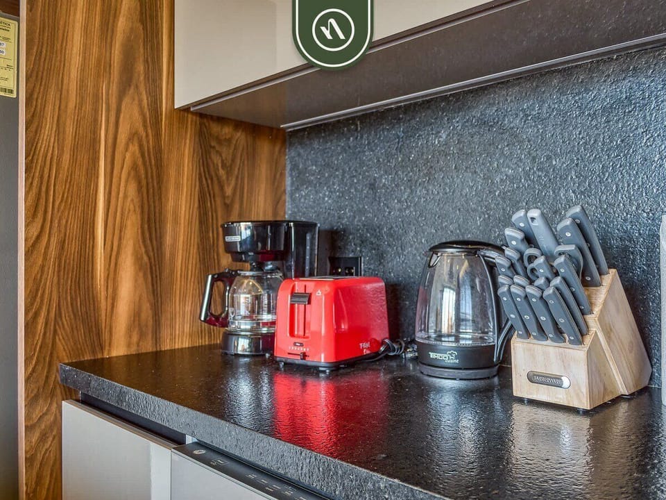 Black kitchen counter equipped with a coffee maker, red toaster, electric kettle, and knife block.