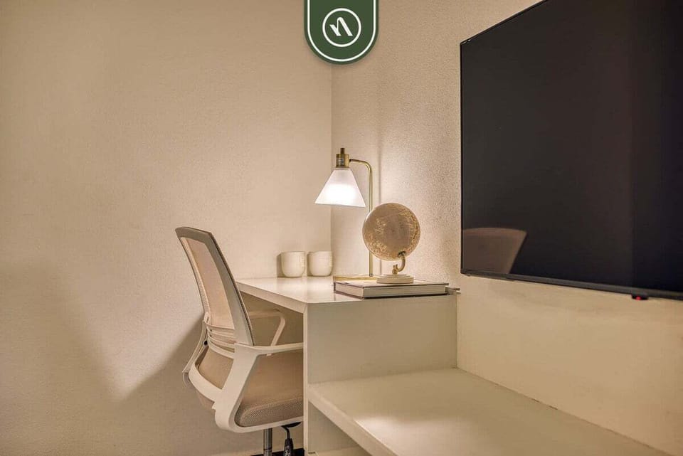 Stay connected at this sleek white study desk featuring a modern mesh office chair, soft task lighting, and a wall-mounted TV.
