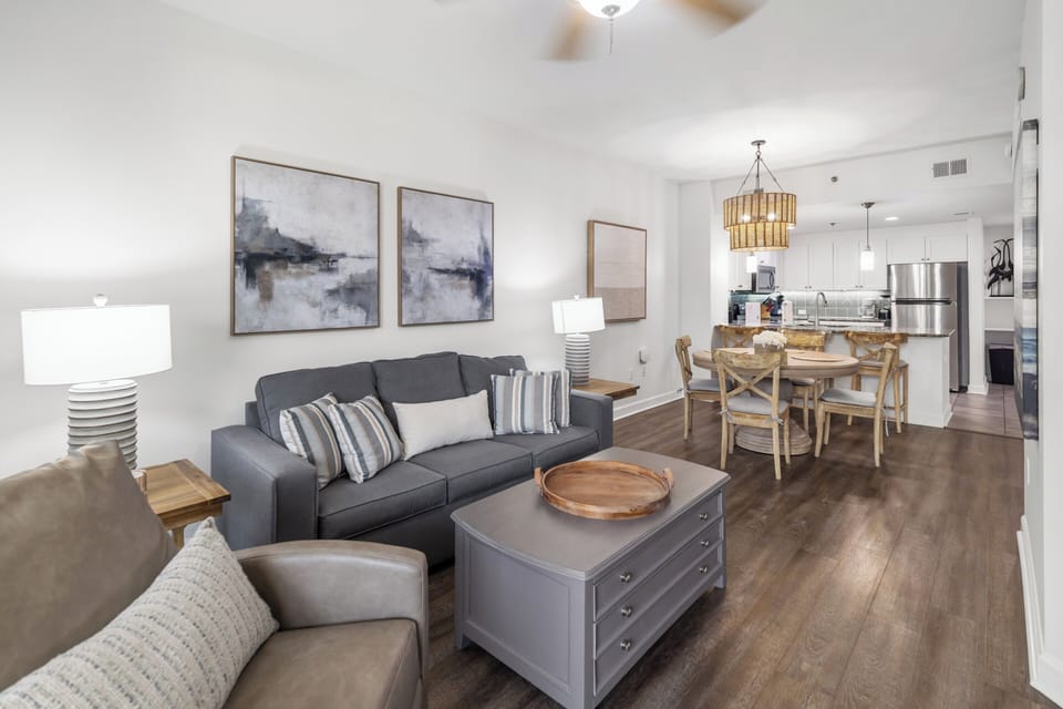 Your open-concept living space welcomes you with airy ceilings, stylish furnishings, and warm wood floors that connect the cozy lounge to the bright kitchen and dining area.