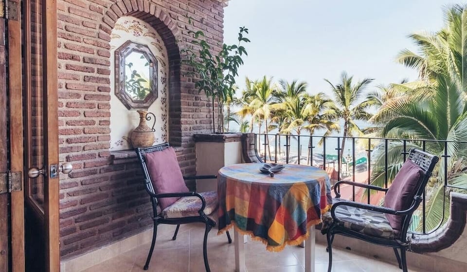 Charming outdoor dining set framed by a classic brick archway, with palm trees and a partial ocean view in the background.