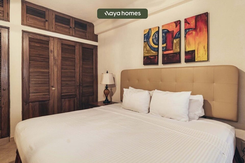 Elegant bedroom setup showcasing a large bed with crisp white linens, matching nightstands, and a multi-paneled abstract wall painting.