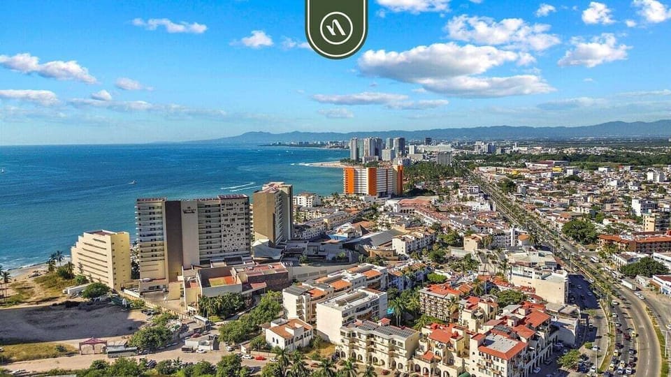 High-angle panorama looking out over the bustling town buildings toward the open blue sea and distant coastline.