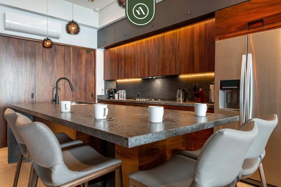 Close-up of a premium granite island counter with comfortable grey bar stools, modern faucets, and rich wood cabinetry.