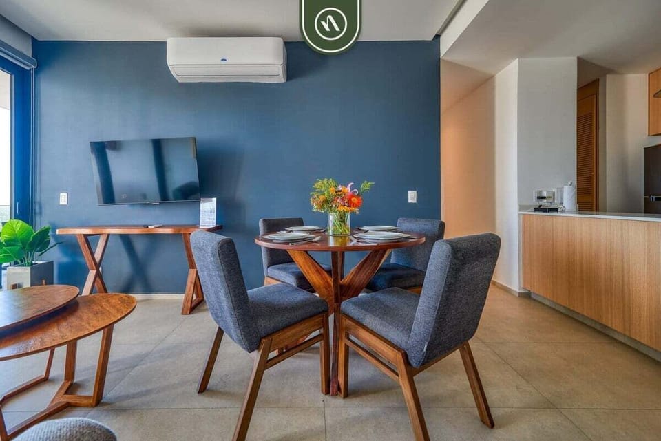Host a meal at the modern wood dining table with plush blue seating. The bold accent wall features a mounted flat-screen TV and a sleek console, perfect for relaxing after dinner.