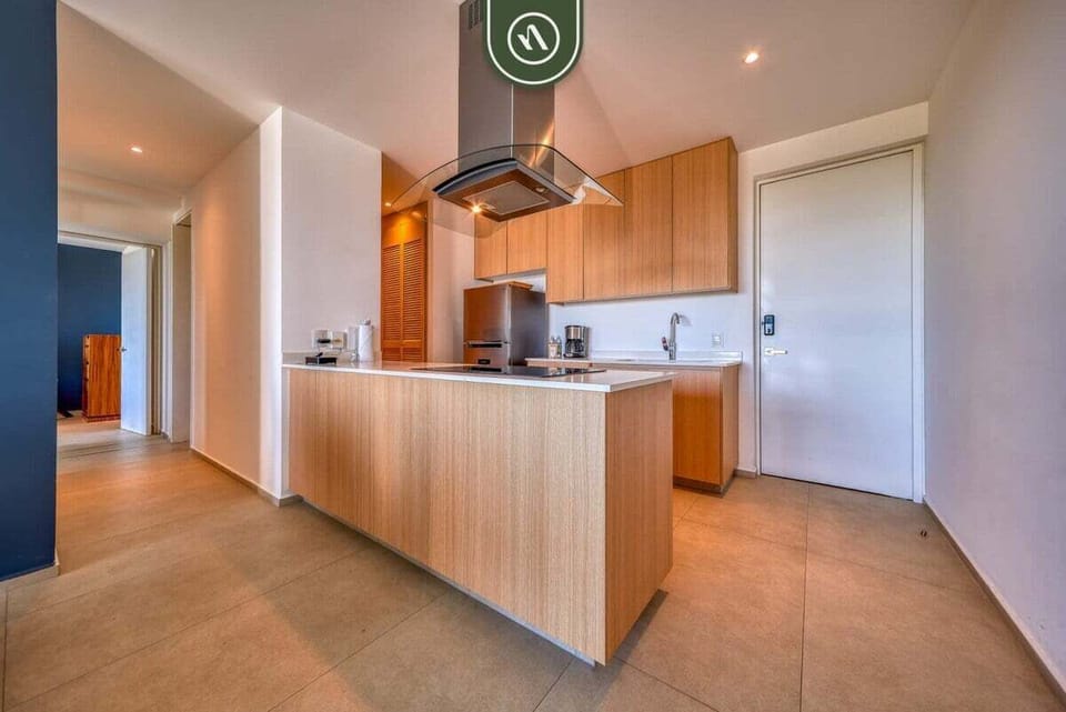 A masterfully designed space featuring light wood cabinetry, a professional-grade exhaust hood, and a sleek island. Perfect for preparing light meals in a modern setting.