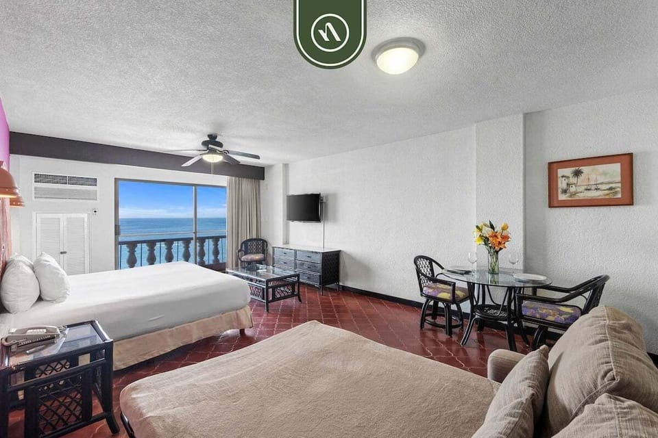 Open-concept guest room featuring a king bed setup, terracotta floor tiles, and a secondary sofa seating area.