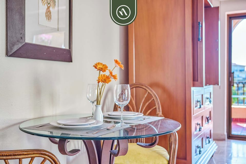 Detailed perspective of a glass-top dining table neatly arranged with fine tableware, wine glasses, and a vibrant orange floral centerpiece.
