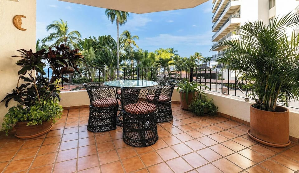 An alternate look at the shaded balcony lounge setup, framed by lush tropical foliage and views of neighboring architecture.
