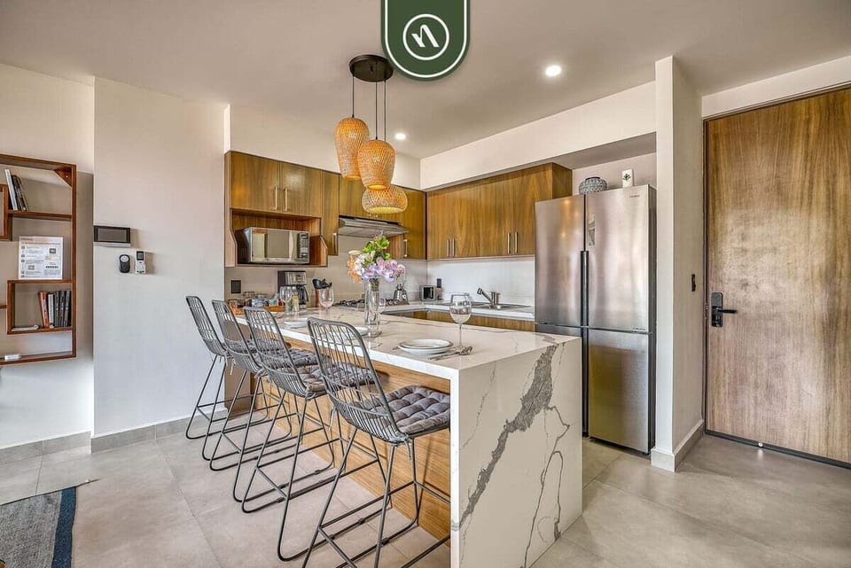Cook and entertain in style. This modern kitchen boasts a stunning waterfall marble island with seating, chic pendant lighting, warm wood cabinetry, and high-quality stainless steel appliances.