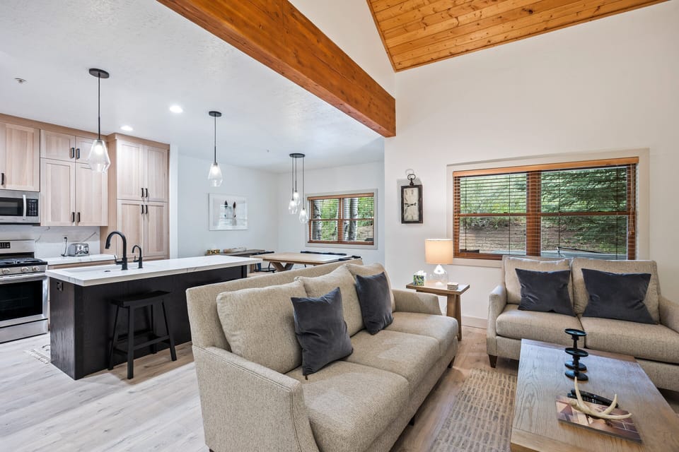 - Open concept living room with modern sofa seating and wood accents  
- Kitchen island with bar stools and stainless steel appliances nearby  
- Large windows bring natural light and forest views into gathering space