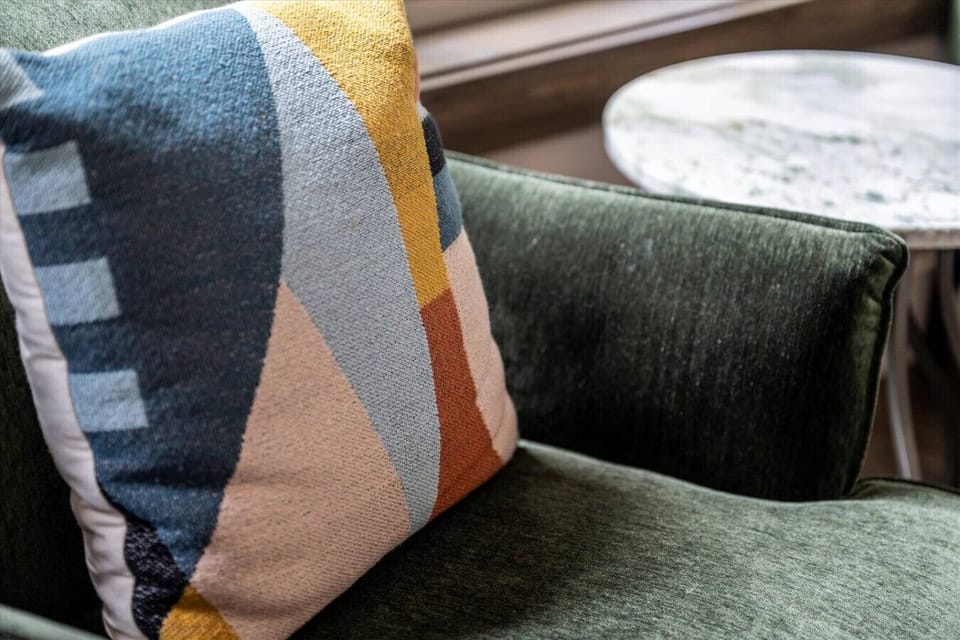Colorful geometric pillows on the deep green armchairs bring a lively pop of character, making this corner as photogenic as it is comfortable.