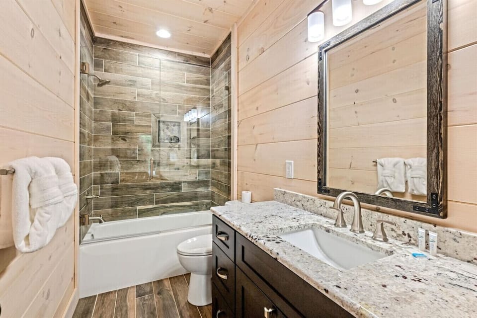 Refresh in the walk-in glass shower surrounded by wood-grain tile, offering both style and comfort after a long day of exploring Pigeon Forge.
