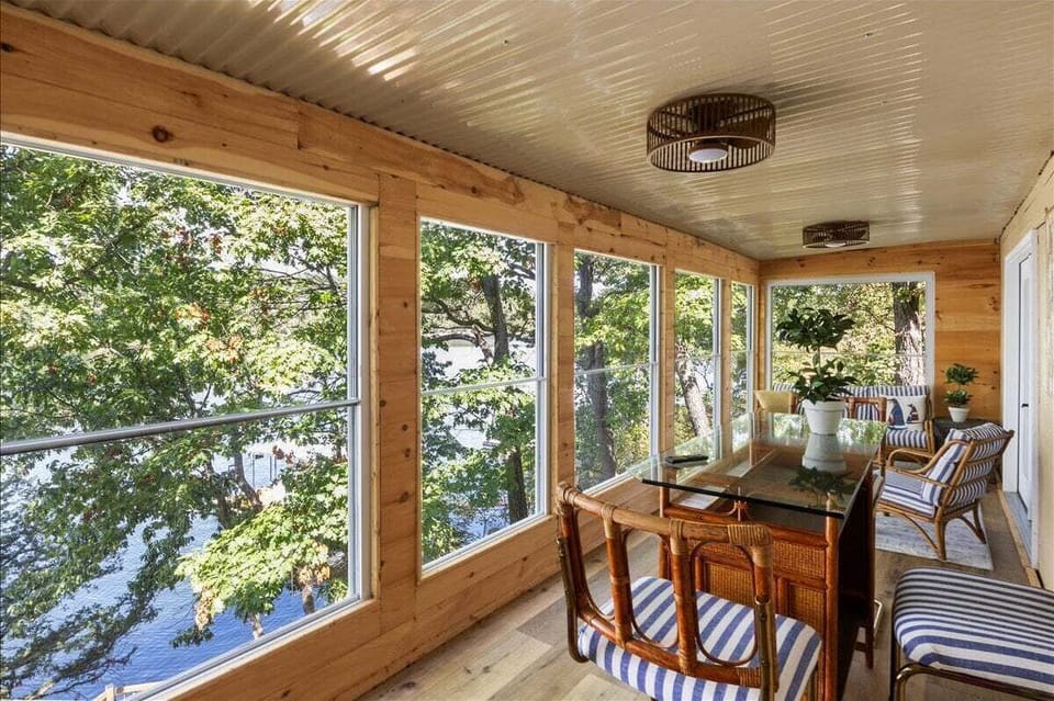 A dining table and bench in the window-lined sunroom provide a scenic spot for meals above the water.