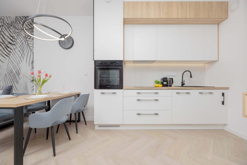 A view of the dining area and kitchen together, showcasing the clean design and practical layout. The wooden cabinets pair beautifully with the modern lighting fixture.