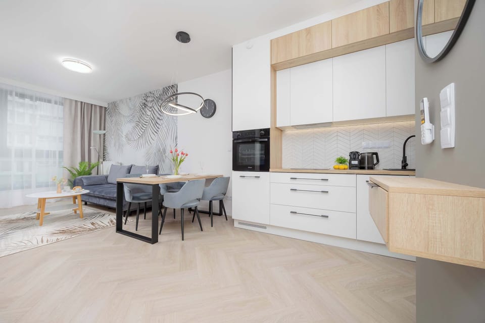 A bright and modern open-plan living area with a round dining table and four stylish chairs. The space seamlessly connects to the fully equipped kitchen.