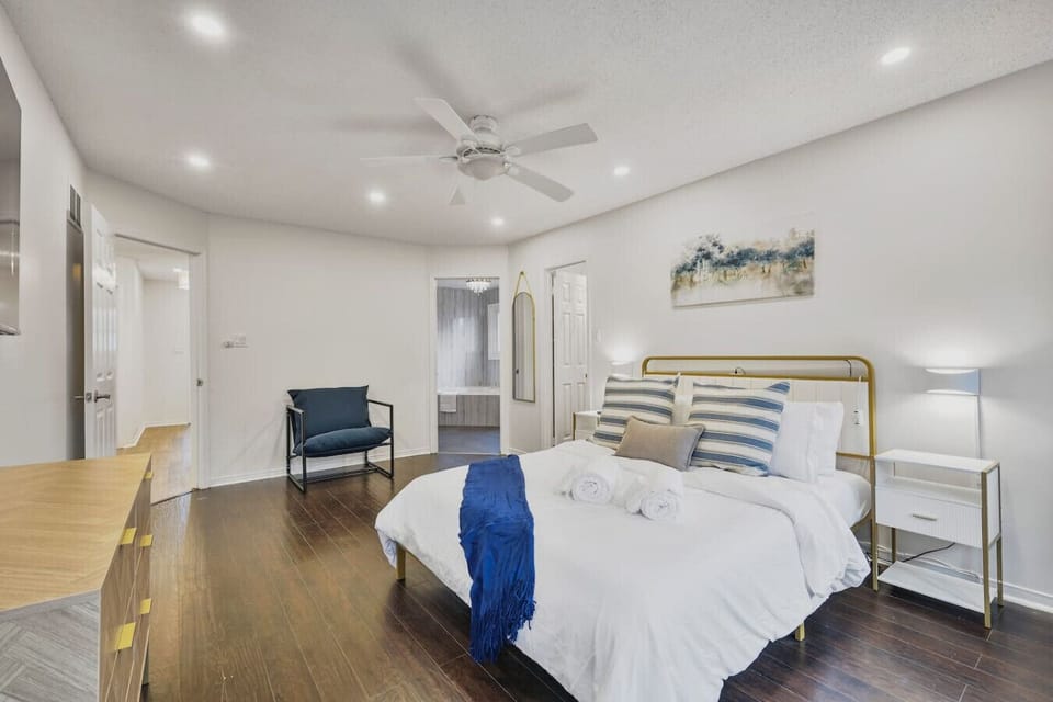 Welcome to the primary suite retreat. This spacious bedroom features a luxe queen bed, rich wood floors, and calming coastal decor. Enjoy the convenience of a comfortable reading nook and direct access to the en suite bathroom.