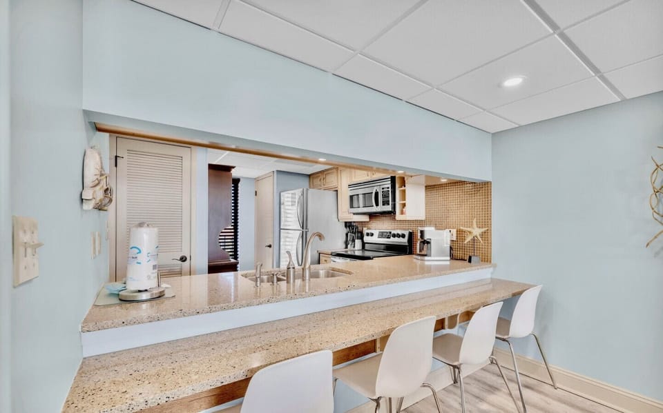 This open-concept kitchen features a granite breakfast bar with seating for four, stainless steel appliances, and coastal charm throughout.