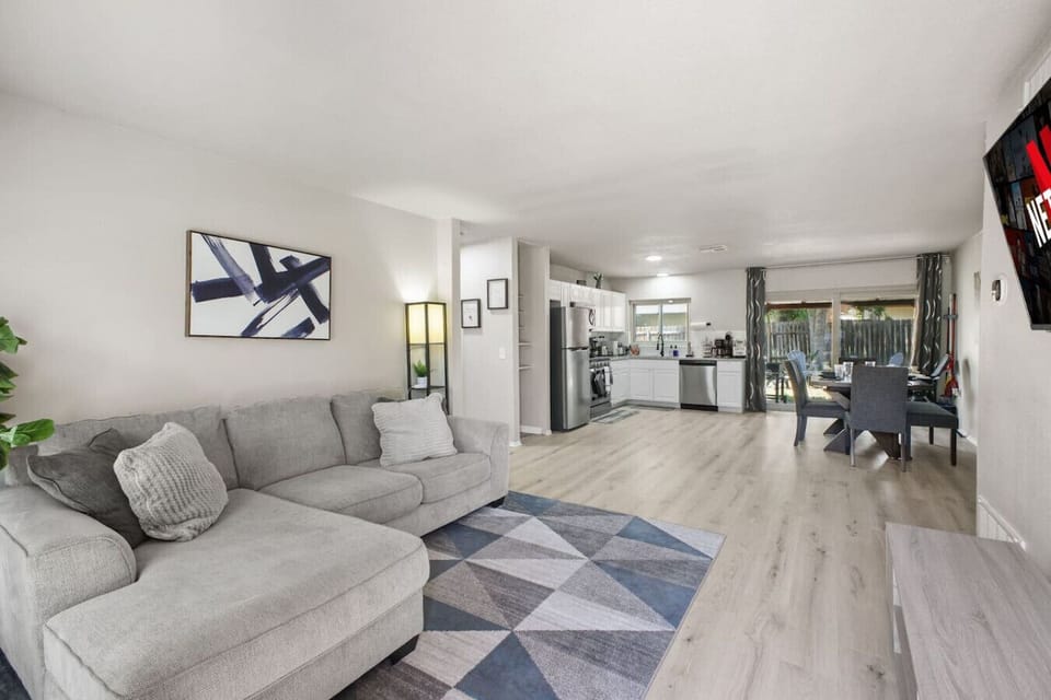 Enjoy a cozy stay in this modern open-concept space featuring a plush sectional, smart TV with Netflix, sleek wood floors, and a fully equipped kitchen with a bright dining area and garden views—perfect for relaxing or entertaining.