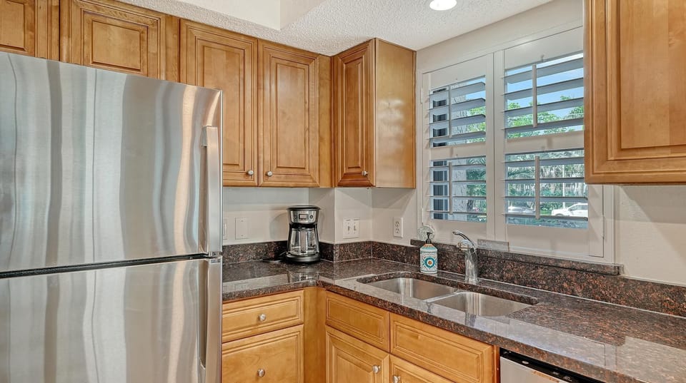Kitchen corner with dark granite countertops, stainless steel fridge, wooden cabinets, and white plantation shutters.