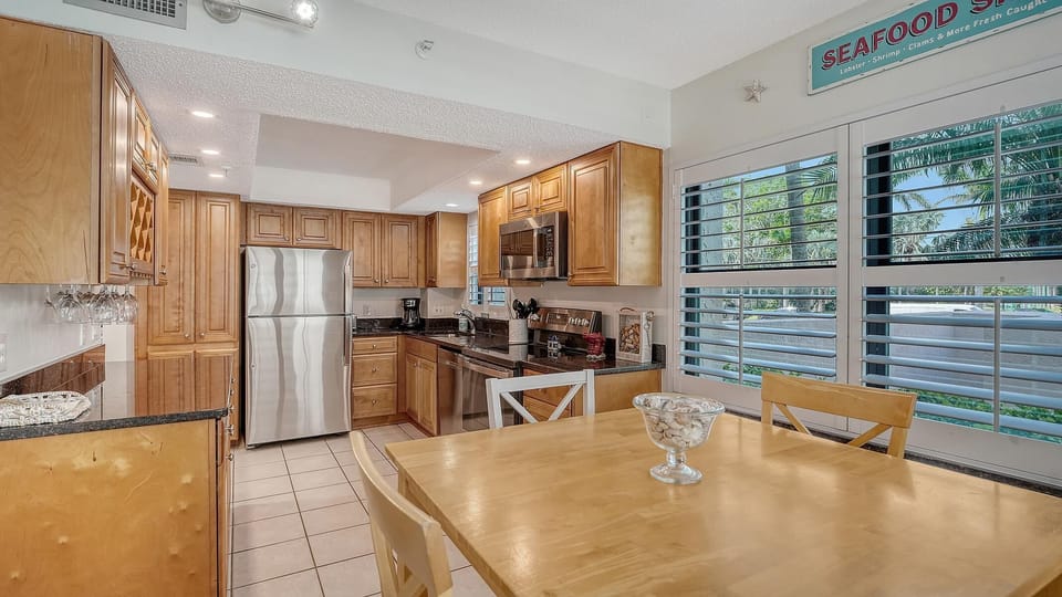 Kitchen and dining area with honey wood cabinetry, black granite counters, stainless steel appliances, and plantation shutters.