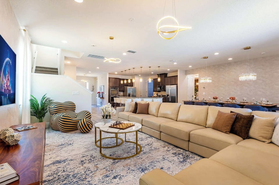 Where the family naturally gravitates after a day at the parks — a sculptural sectional for sixteen, anchored by a designer chandelier, opening seamlessly to the chef's kitchen beyond.