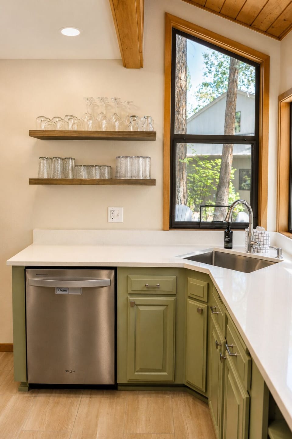 Your well-appointed kitchen features warm wood accents, open shelving for glassware, and a view of the surrounding pines through the large window above the sink.
