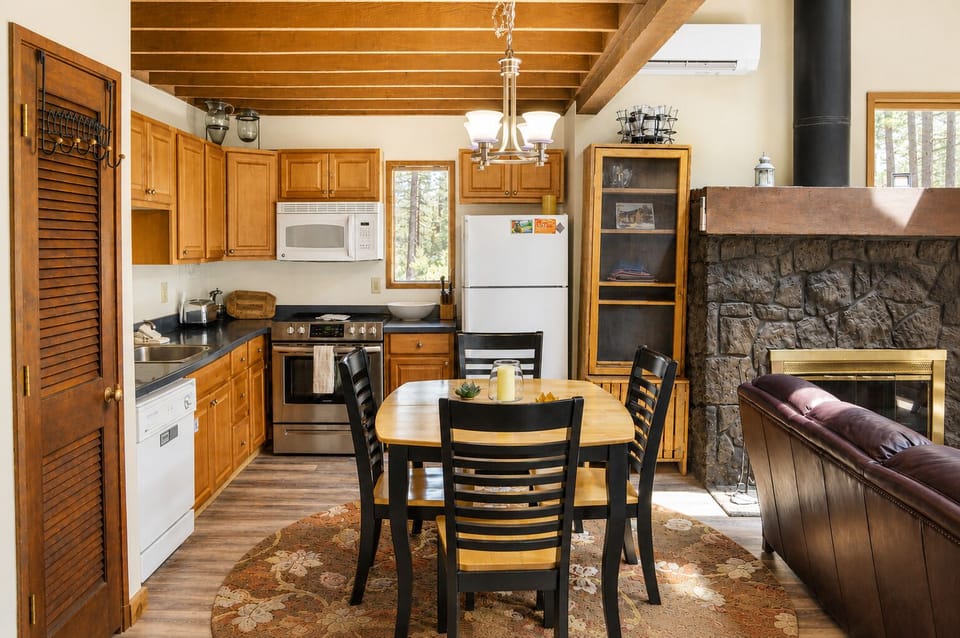 Gather around the dining table in this warm, open-concept space where exposed beams meet modern convenience. Your fully equipped kitchen invites meal prep, while the stone fireplace creates cozy ambiance for memorable evenings together.
