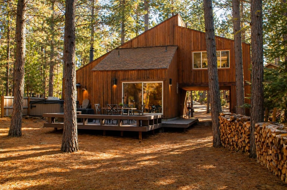 Modern cedar cabin nestled among towering pines, featuring spacious deck for outdoor dining and relaxation in nature's embrace.