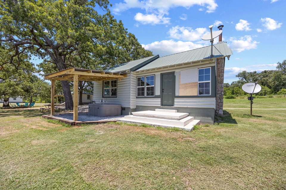 Charming cabin with a green metal roof, shaded patio, and peaceful country views.