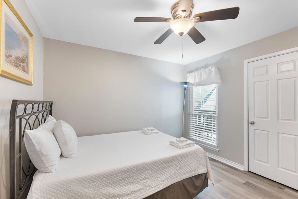 Sink into crisp white linens in your peaceful bedroom, where soft natural light and gentle ceiling fan create the perfect retreat.