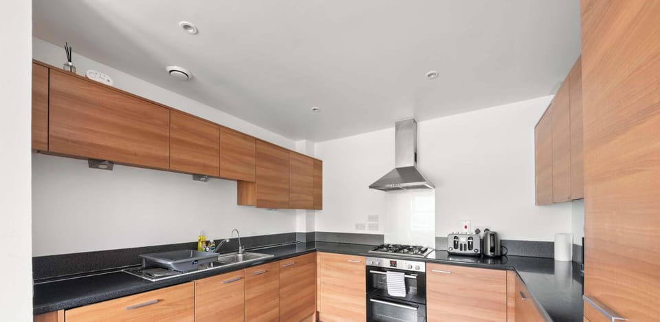 This modern kitchen is designed for both style and efficiency, offering a spacious layout that is perfect for any home cook. The warm wood-finish cabinetry provides a beautiful contrast against the dark slate-grey countertops and large floor.
