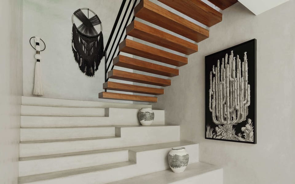 Floating concrete staircase with black iron railing and Oaxacan folk art on white wall.