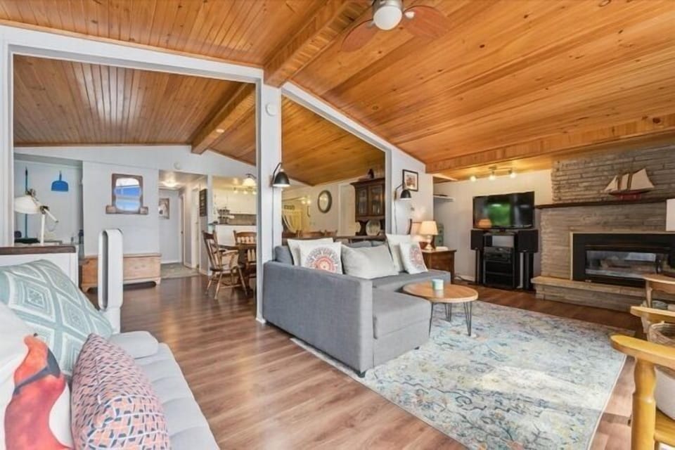 Warm and inviting open-concept living space with wood-paneled vaulted ceilings, cozy seating, and charming cottage décor.