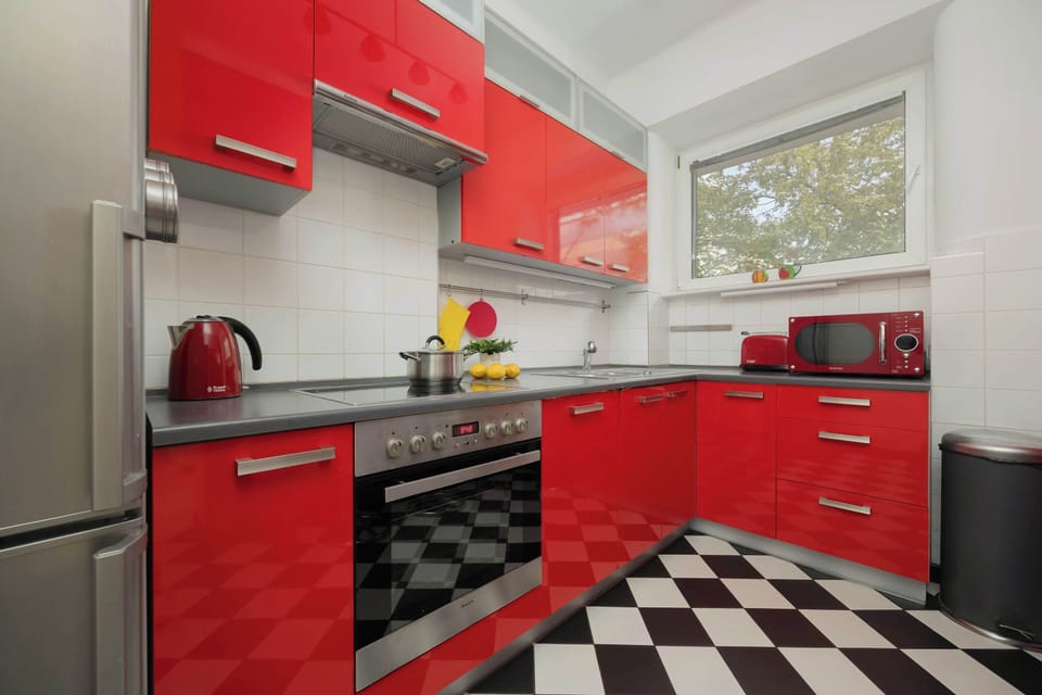 A modern kitchen featuring bold red cabinetry, black-and-white checkered flooring, and stainless steel appliances.
