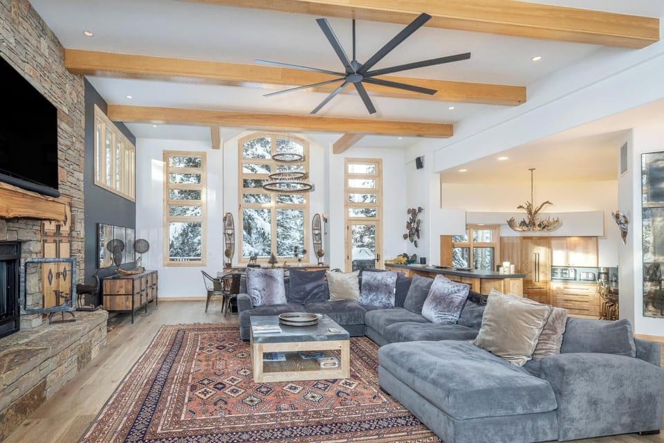 Relax in your spacious living room featuring exposed wood beams, a stone fireplace, and plush sectional seating that flows seamlessly into the gourmet kitchen.