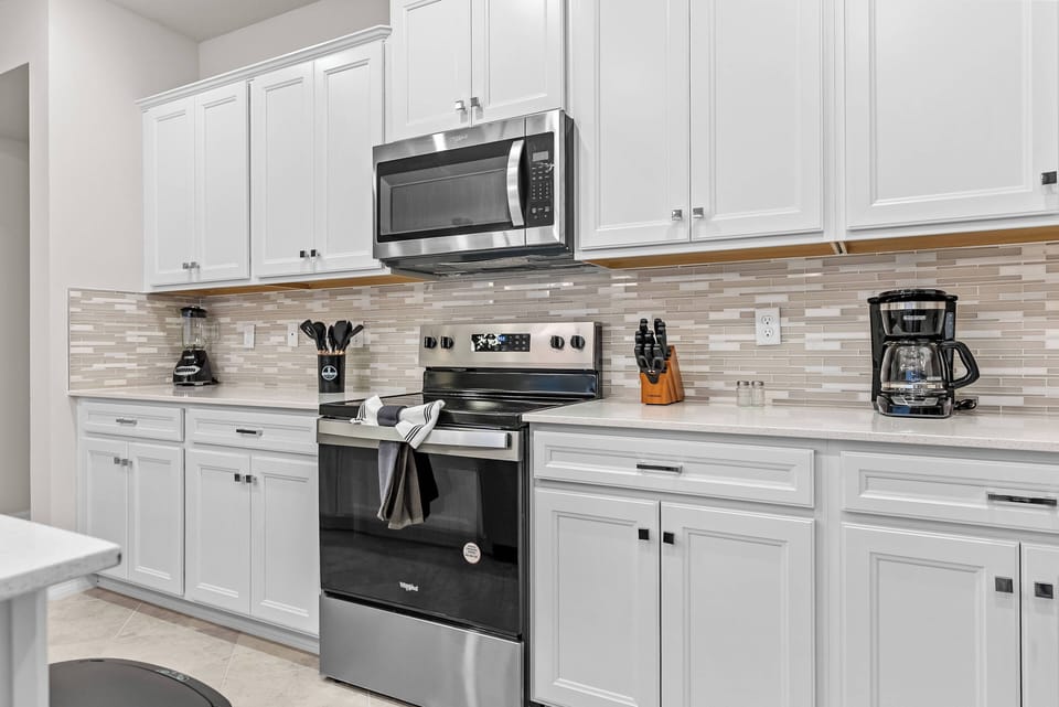 This bright kitchen boasts sleek white cabinetry and a stylish warm-toned tiled backsplash, creating an airy ambiance. With modern stainless-steel appliances, it offers a convenient cooking experience during your stay.