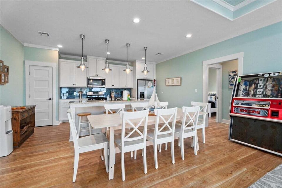 Coastal dining room with oversized table, bright kitchen, pendant lighting, and open layout designed for family meals and entertaining.