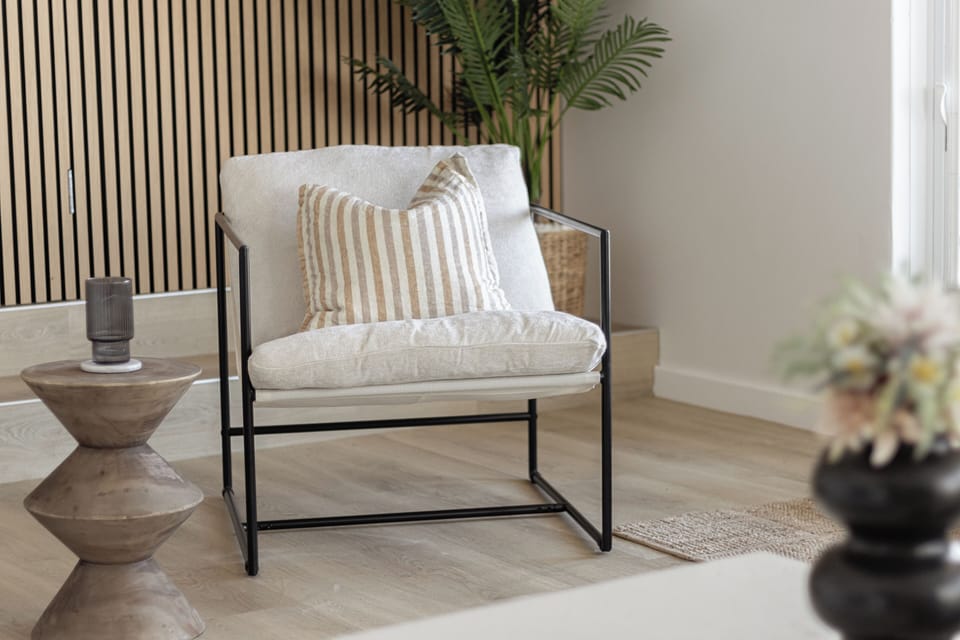 Find your perfect reading nook in this stylish and inviting corner. Sink into the comfortable armchair, accented with a chic striped pillow, and enjoy the natural light filtering in. A unique side table provides a spot for your drink or book.