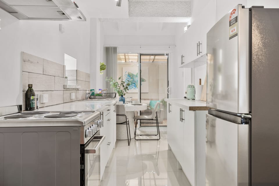 Prepare delicious meals in our bright and modern kitchen, fully equipped for your cooking needs. Featuring sleek white cabinetry, ample countertop space, and stainless steel appliances including a refrigerator and oven.