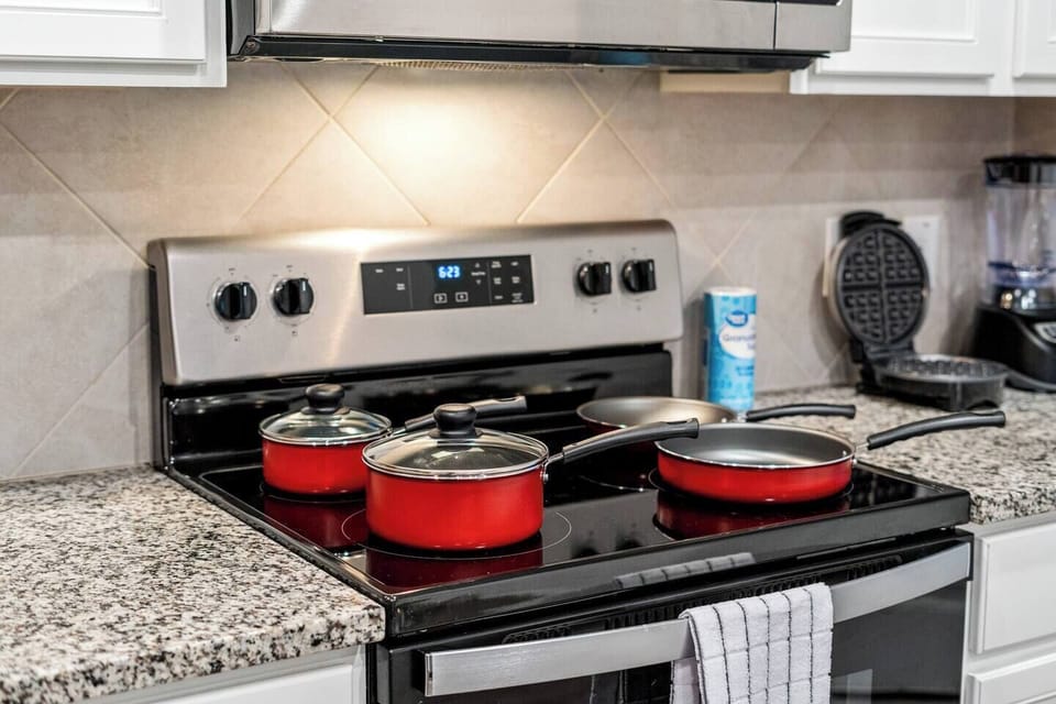 Fully equipped kitchen w modern appliances and red cookware, perfect for preparing meals. Includes extras like waffle maker for added convenience. Ideal for long-term guests who enjoy cooking and want comfort of a home-cooked meal during their stay.