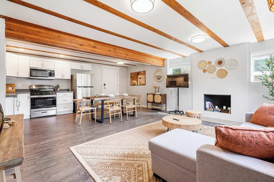 Living room with dual focal points​ showcasing a movable TV stand, opposite a sunlit conversation area with circular nesting tables on geometric rug.​