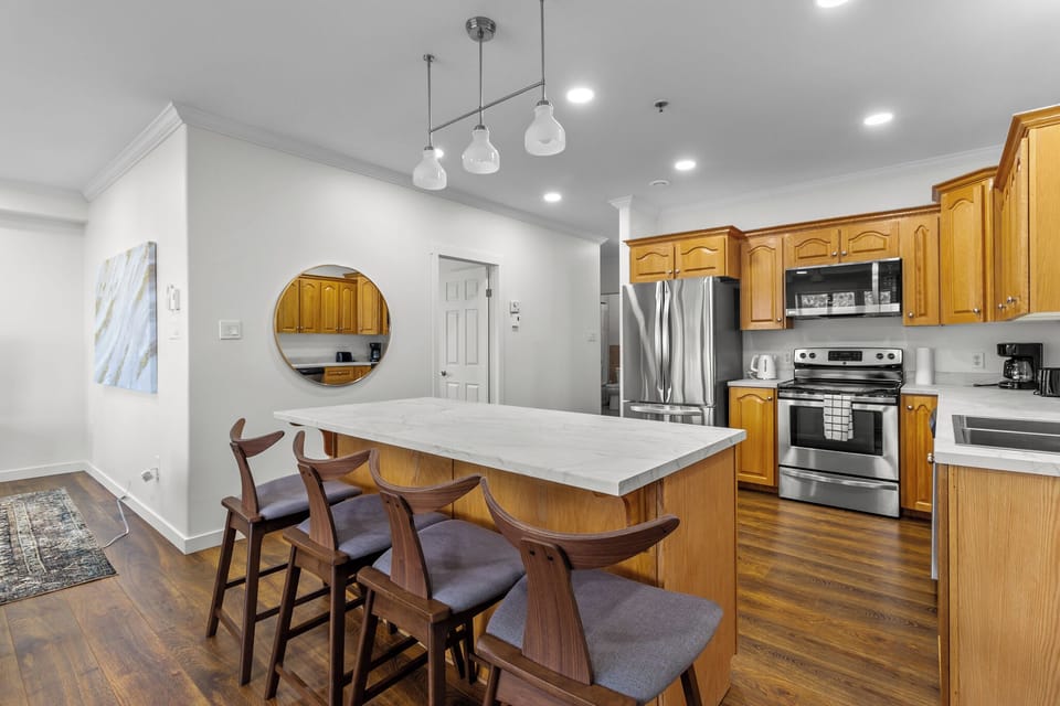 Modern kitchen with wooden cabinets, stainless steel appliances, and a large marble island with seating for four.