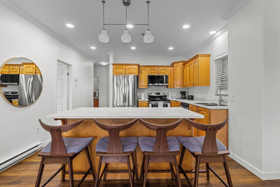 Spacious kitchen featuring wooden cabinetry, stainless steel appliances, and a large marble island with seating for four.