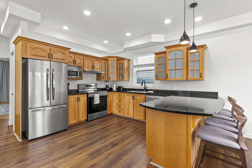 Fully equipped kitchen with modern stainless steel appliances, ample wooden cabinetry, and a sleek black countertop. Perfect for cooking and entertaining.