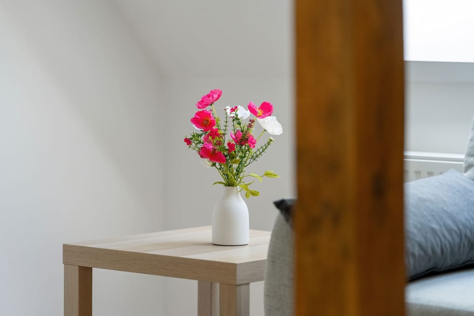 A decorative detail of a small table with a vase of pink flowers. The minimal setup brightens the otherwise neutral room.
