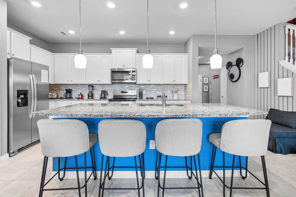 This bright kitchen with sleek white cabinets and a vibrant blue island is ideal for casual dining, featuring modern stainless steel appliances and stylish pendant lighting that create a warm, inviting atmosphere for your stay.
