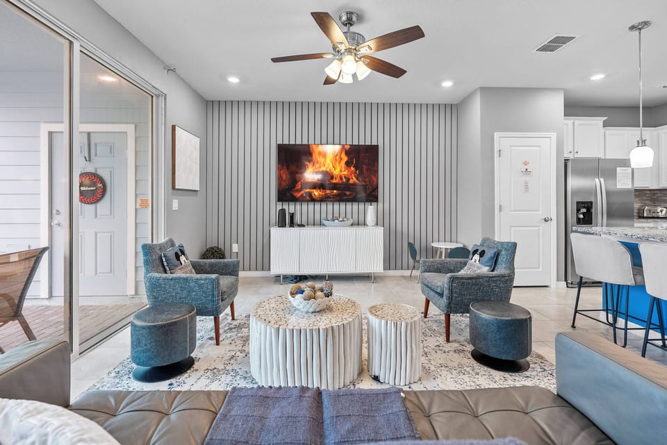 Relax in this stylish living room with textured gray walls, cozy seating around a chic coffee table, and a large flat-screen TV for entertainment. A ceiling fan adds a gentle breeze for your comfort.