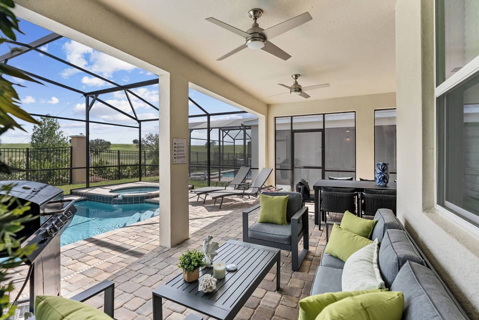 Step into a shaded outdoor lounge where modern furniture meets vibrant green accents. With ceiling fans for comfort and a view of the inviting pool, this space is perfect for relaxing or entertaining in style.