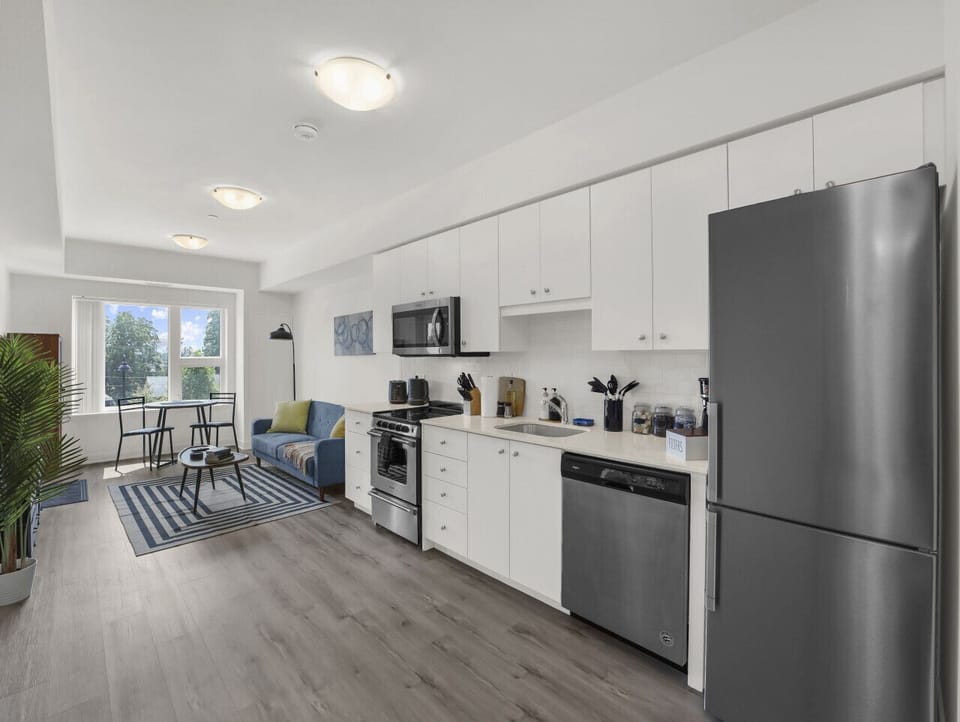 A bright, modern space awaits. Enjoy stylish white cabinets, stainless steel appliances, and a comfortable living area with natural light. Your perfect stay starts here.